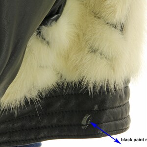 May include: Close-up of a black leather jacket with a white fur collar. The jacket has a visible area where the black paint has rubbed off.