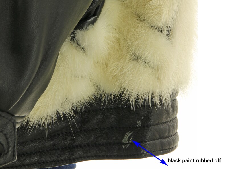 May include: Close-up of a black leather jacket with a white fur collar. The jacket has a visible area where the black paint has rubbed off.