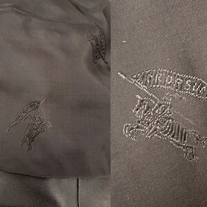 May include: Close-up of a black fabric with a repeated embroidered design of a knight riding a horse with a flag that says "BURBERRY".