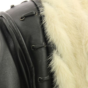 May include: Close-up of a black leather jacket with a white fur collar. The jacket has a zipper closure and a decorative lacing detail.