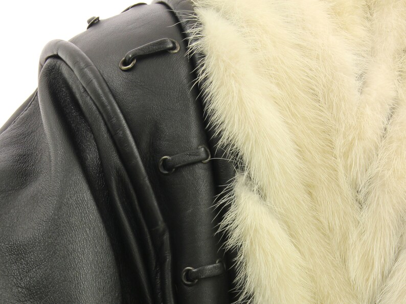 May include: Close-up of a black leather jacket with a white fur collar. The jacket has a zipper closure and a decorative lacing detail.