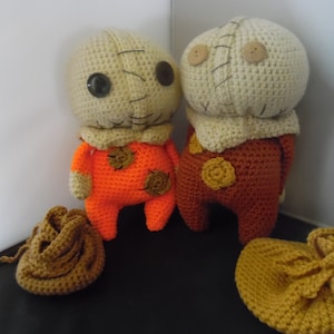 May include: Two crocheted stuffed toys with stitched faces and button eyes. One is orange with brown accents and the other is brown with beige accents. Both are wearing crocheted hats.