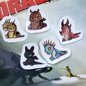 May include: A collection of five cartoon dragon stickers in various colors. The stickers feature dragons with different designs, including a two-headed yellow dragon, a brown dragon, a red dragon, a black dragon, and a blue dragon. The stickers are on a white background.