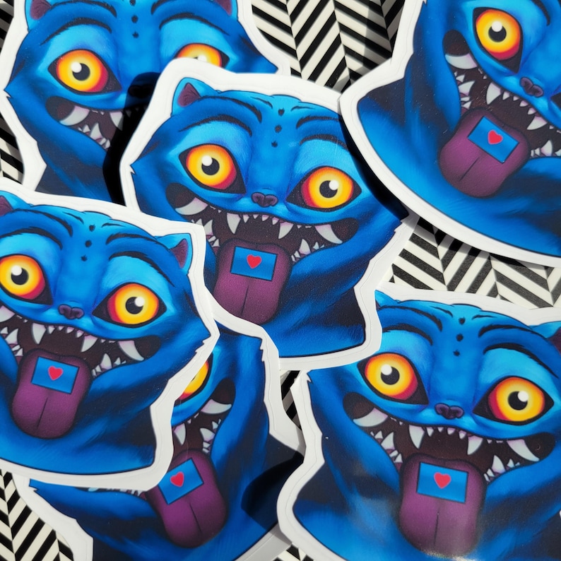 Op de afbeelding: Een verzameling blauwe kattenstickers met open monden, scherpe tanden en uitgestoken tongen. De tongen zijn paars met een kleine blauwe rechthoek en een rood hart. De katten hebben gele en oranje ogen.