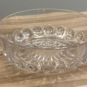 May include: A clear glass bowl with a textured, raised design around the rim and base. The bowl is empty and sitting on a wooden surface.