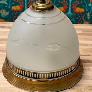 May include: A vintage light fixture with a frosted glass shade and brass base. The shade is dome-shaped with etched floral details and horizontal etched lines. The brass base has a decorative design.