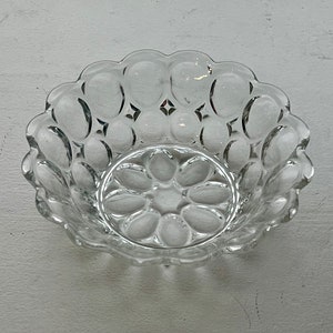 May include: A clear glass bowl with a scalloped edge and a pattern of raised circles. The center of the bowl features a floral design. The bowl is likely used for serving or display.