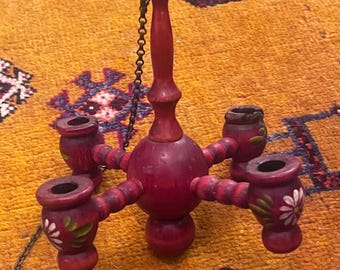 Puede incluir: Una lámpara de araña de madera roja con cuatro candelabros. Cada candelabro tiene un diseño de flor blanca pintada. La lámpara de araña está colgada de una cadena.