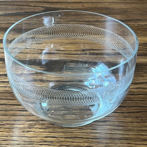 Könnte beinhalten: Eine klare Glasschüssel mit einem dekorativen, geätzten Design aus wirbelnden Linien. Die Schüssel steht auf einer Holzoberfläche.