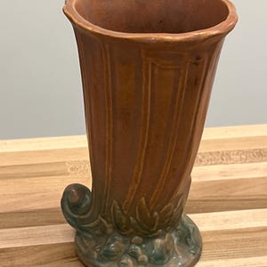 May include: A brown and green ceramic vase with a fluted design and a leafy base.