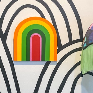 May include: A colorful rainbow arch with yellow, orange, green, red, and pink stripes against a black and white striped background.