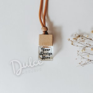 May include: A small, clear glass bottle with a wooden top and a brown cord. The bottle has a label that says "Your Design Here". The bottle is on a white background with a sprig of dried flowers.