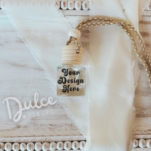 Puede incluir: Una botella de vidrio transparente con una tapa de madera y una etiqueta blanca que dice "Your Design Here". La botella está colgada de un cordón marrón y está sobre una superficie de madera blanca con una tela blanca.