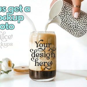 May include: A glass can with a black and white design that says "Your design here" is being filled with milk from a white jug with black polka dots. The can is sitting on a white surface with a wooden lid and white flowers.