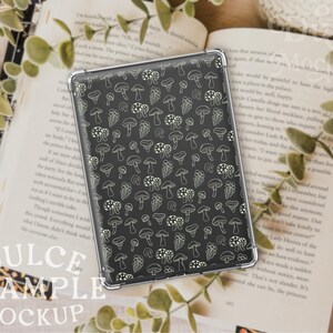 May include: A black phone case with a white mushroom pattern. The case is lying on a book with green leaves.