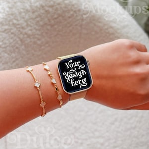May include: A gold smartwatch with a black screen displaying the text "Your design here" is worn on a wrist, next to two gold bracelets with heart and clover charms. The watch has a gold mesh band.