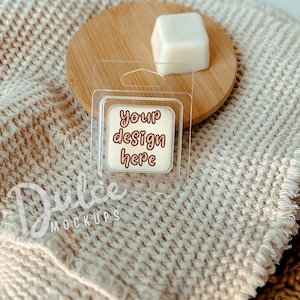 May include: A clear plastic container with a white wax melt inside. The wax melt has the text "your design here" printed on it. The container is sitting on a brown woven blanket.