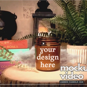 Peut inclure: Un bocal de bougie en verre ambré avec le texte "your design here" sur une surface en bois avec une plante verte et des livres en arrière-plan. Le texte "mockup video" est également visible sur l'image.