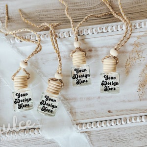 May include: Four clear glass bottles with wooden tops and strings. Each bottle has a label that says "Your Design Here". The bottles are on a white wooden surface with a white beaded trim.