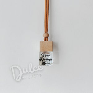 Könnte beinhalten: Ein braunes Band hängt an einer quadratischen Flasche mit einem Holzdeckel und einem Glaskörper. Die Flasche trägt den Text "Your Design Here".