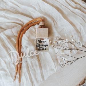 May include: A small glass bottle with a wooden top and a brown cord. The bottle is filled with a clear liquid and has the text "Your Design Here" printed on it. The bottle is sitting on a white fabric surface.