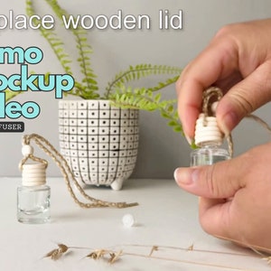 Könnte beinhalten: Nahaufnahme einer Hand, die den Holzdeckel eines klaren Glas-Autodiffusors durch einen weißen Holzdeckel ersetzt. Der Diffusor hängt an einer braunen Schnur. Der Text "Replace wooden lid demo mockup video CAR DIFFUSER" ist oben im Bild sichtbar.