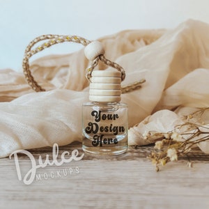 May include: A clear glass bottle with a wooden cap and a gold string. The bottle is filled with a clear liquid and has a label that says "Your Design Here". The bottle is sitting on a wooden surface with a piece of fabric and dried flowers.