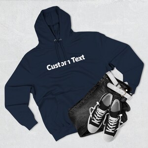May include: A navy blue hoodie with the text "Custom Text" in white, paired with dark denim jeans, a white belt, and black and white sneakers. The hoodie has a drawstring hood and a front pocket.