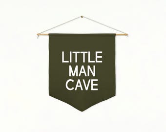 May include: A dark green banner with the words "LITTLE MAN CAVE" in white block letters. The banner is suspended from a wooden rod with a string. The text "Pine + White Text" is at the bottom.
