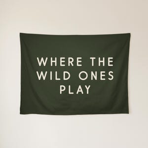 May include: A rectangular dark olive green wall tapestry featuring the white text WHERE THE WILD ONES PLAY centred in a clean sans-serif font. The fabric has a smooth texture and hangs horizontally with a simple, minimalist aesthetic.