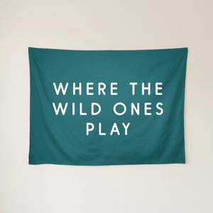 May include: A rectangular teal wall tapestry featuring the white text WHERE THE WILD ONES PLAY centred in a clean sans-serif font. The fabric has a smooth, matte finish and hangs flat against the wall, displaying clear, bold lettering.