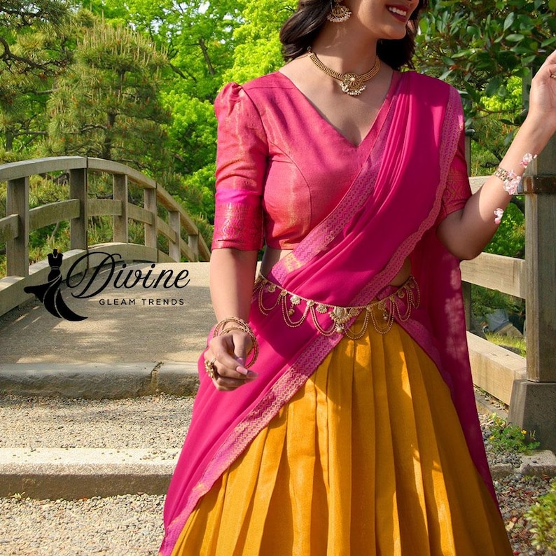 May include: A woman wearing a traditional Indian outfit. The ensemble features a pink blouse and draped fabric, paired with a yellow skirt. A gold belt and jewelry complete the look. The image includes the text "Divine Gleam Trends".