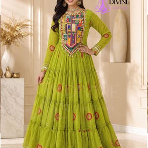 May include: A lime green floor-length tiered dress featuring long sleeves and a vibrant, multi-colored embroidered panel on the chest. The fabric is adorned with small white dots and circular red and orange patterns throughout the skirt and sleeves.