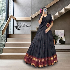 Könnte beinhalten: Ein schwarzes traditionelles indisches Outfit mit einem plissierten Rock und einem drapierten Oberteil. Der Rock hat einen rot-goldenen Saum. Das Outfit wird mit Goldschmuck getragen. Das Logo "Divine Gleam Trends" ist sichtbar.