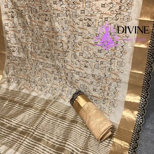 May include: Off-white fabric with a repeating pattern of small figures in brown and black. The fabric has gold stripes and a gold border. The edge is trimmed with black lace. A rolled-up section of the fabric is visible.
