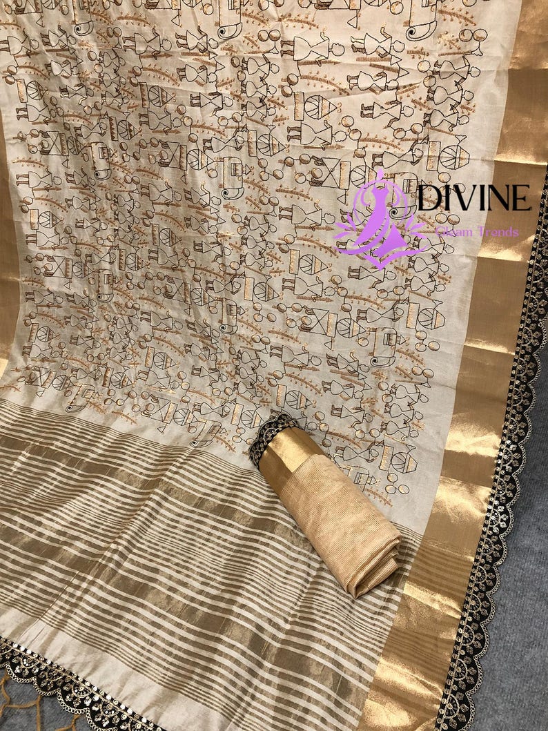 May include: Off-white fabric with a repeating pattern of small figures in brown and black. The fabric has gold stripes and a gold border. The edge is trimmed with black lace. A rolled-up section of the fabric is visible.