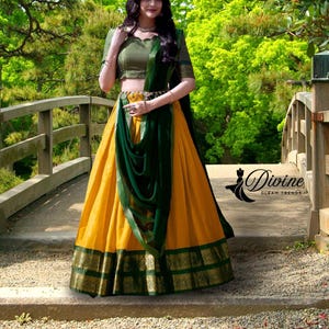 May include: A traditional Indian outfit featuring a mustard yellow skirt with a green and gold border, paired with a green top and a matching green scarf. The outfit is accessorized with a gold belt. The image includes the text "Divine Gleam Trends".