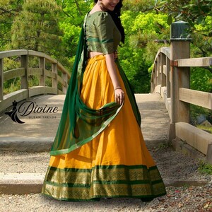 May include: A traditional Indian outfit featuring a yellow skirt with a green and gold border, paired with a green blouse and a matching green scarf. The outfit is adorned with gold accents and the text "Divine Gleam Trends".