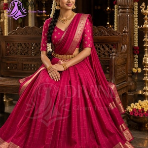 May include: A vibrant magenta lehenga choli featuring a gold checkered pattern and intricate gold zari borders. The ensemble includes a matching blouse with short sleeves, a pleated skirt, and a gold waist belt, accented by gold jewelry.
