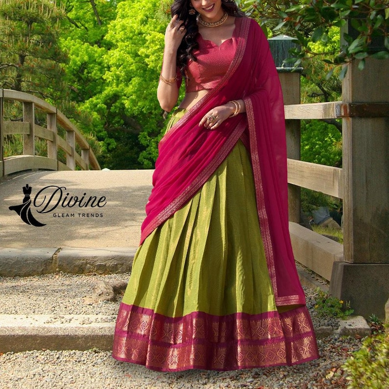 May include: A traditional Indian outfit featuring a green skirt with a patterned border, a pink top, and a matching pink scarf. The outfit is worn by a person standing on a bridge. The text "Divine Gleam Trends" is visible.