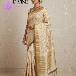 May include: A cream-colored sari with gold and black accents. The sari features intricate patterns and a gold border. The text "DIVINE Gleam Trends" is visible in the upper left corner. The sari is draped on a person.