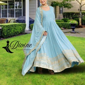 May include: A light blue, floor-length dress with gold embellishments and a matching scarf. The dress features a round neckline and long sleeves. The text "Divine Gleam Trends" is visible on the left side of the image.