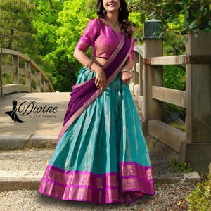 May include: A traditional Indian outfit featuring a teal skirt with a magenta and gold border, paired with a magenta blouse and a purple shawl. The outfit is embellished with gold accents and intricate patterns. The brand logo "Divine Gleam Trends" is visible.