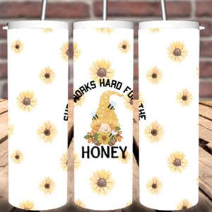 May include: White tumbler with a sunflower pattern and a gnome graphic. The gnome is wearing a yellow hat with bees and holding a sunflower. The text on the tumbler reads "Cute Gnome Works Hard For The Honey".