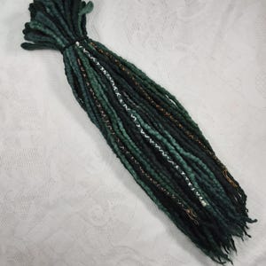 May include: A set of dark green and black wool dreadlocks with gold and white accents. The dreadlocks are tied together at the top.