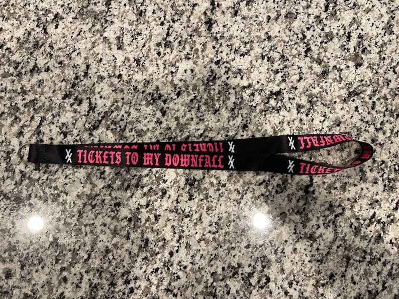 Puede incluir: Lanyard negro con texto rosa que dice "X TICKETS TO MY DOWNFALL X".