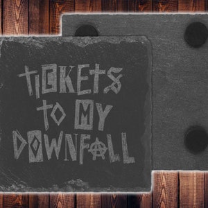 May include: Two black slate coasters with cork backing. The top coaster has the text "Tickets to my Downfall" written in white.