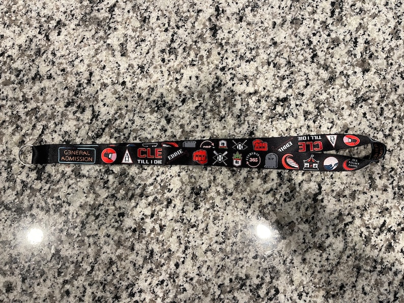 Puede incluir: Lanyard negro con texto rojo y blanco que dice "General Admission" y "CLE TILL I DIE". El lanyard tambi&eacute;n presenta varios gr&aacute;ficos, incluyendo una calavera, un bate de b&eacute;isbol y una ola.