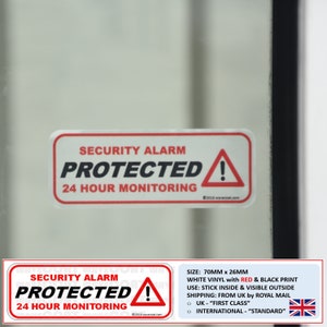 Op de afbeelding: Witte vinyl beveiligingsalarm sticker met rode en zwarte print. De sticker heeft de tekst "Security Alarm Protected! 24 Hour Monitoring" met een rood uitroepteken in een witte driehoek. De sticker is 70 mm x 26 mm.
