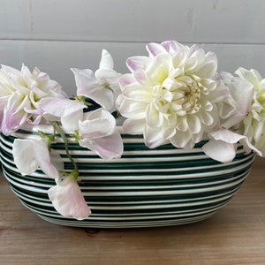 May include: A white and green striped ceramic vase with white and pink flowers. The vase is oval shaped and has a glossy finish.